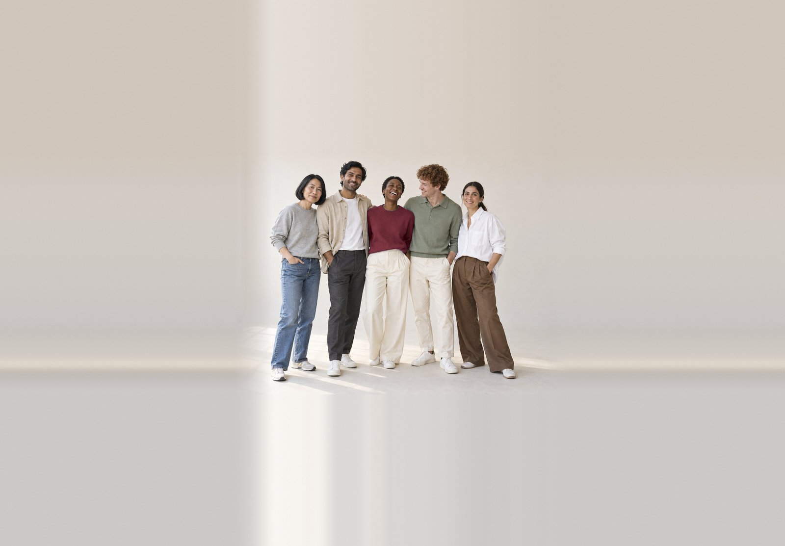 Five friends laughing together in Halcy autumn pieces: a grey marl sweatshirt, an oat overshirt, an oxblood crew, a sage knitted polo and a white poplin shirt